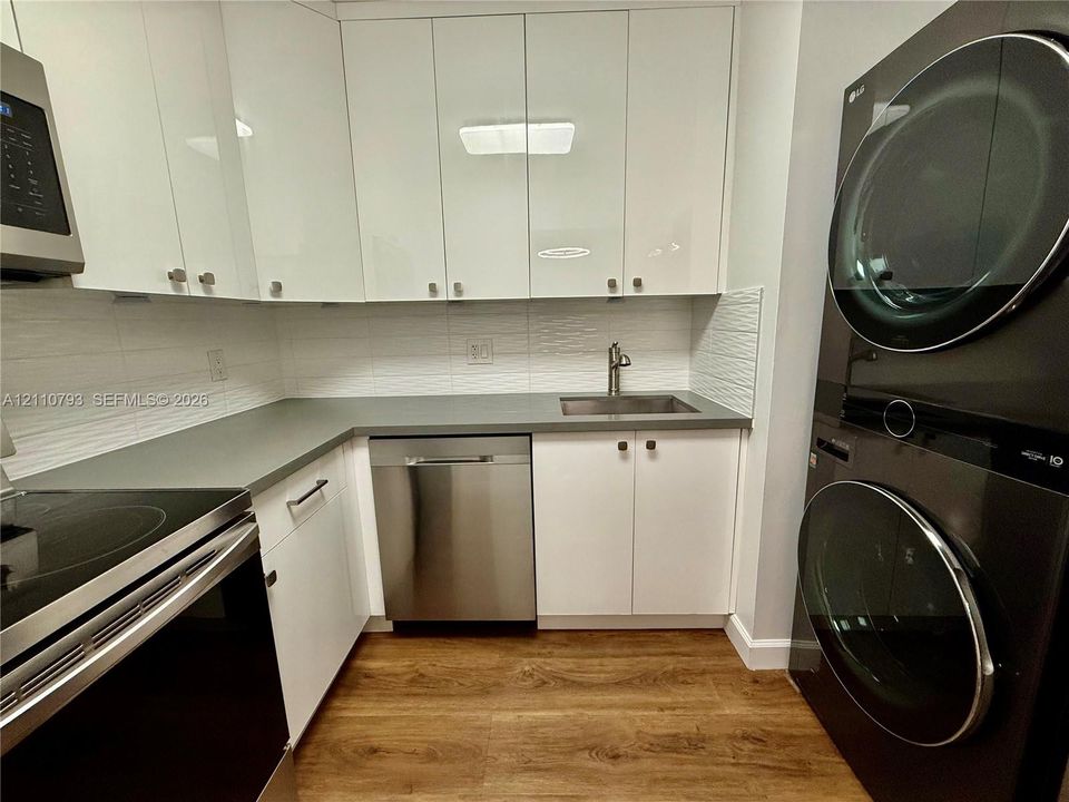 High-gloss white cabinetry, solid-surface countertops, integrated stainless steel dishwasher, undermount sink with metal faucet, and wood-finish flooring