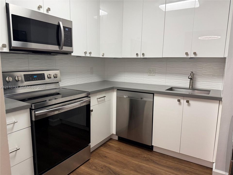 Kitchen featuring white slab cabinetry, grey solid-surface countertops, stainless steel appliances, a textured tile backsplash, and wood-finish flooring
