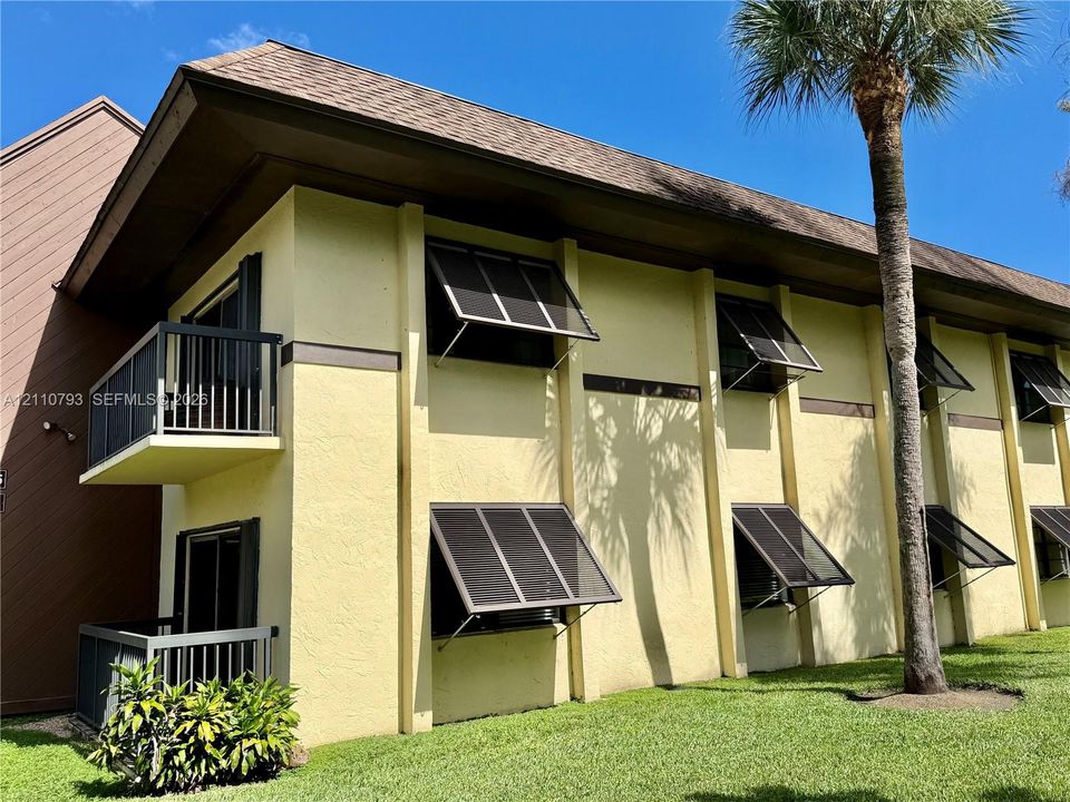 Multi-story stucco exterior featuring prominent vertical architectural pilasters, metal balcony railings, and exterior awning-style window shutters