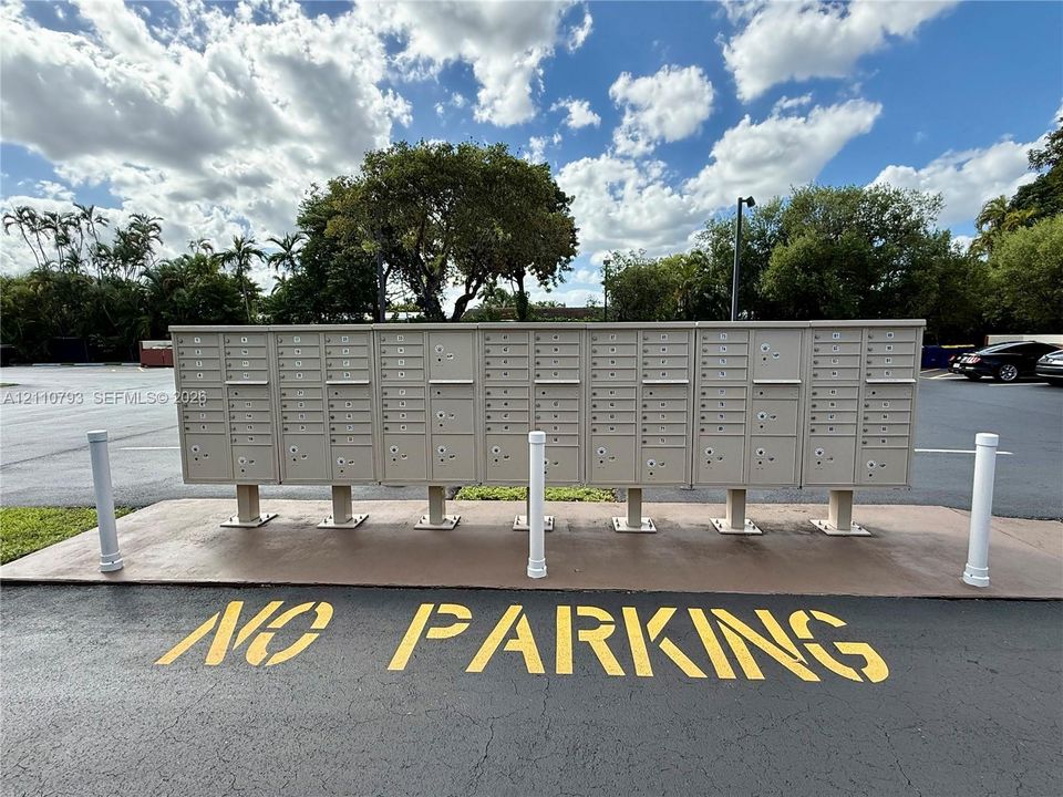 Outdoor cluster mailbox unit mounted on a concrete pad with white metal safety bollards