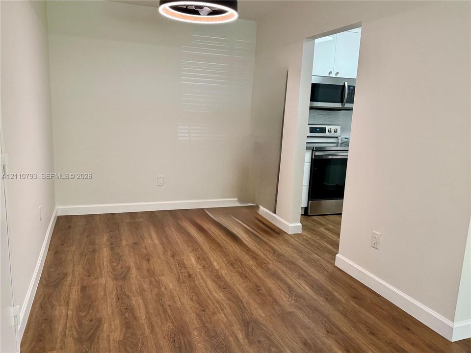 Wood-finish flooring, contemporary circular LED light fixture, and neutral wall color, featuring an open entry to a kitchen equipped with stainless steel appliances and white cabinetry