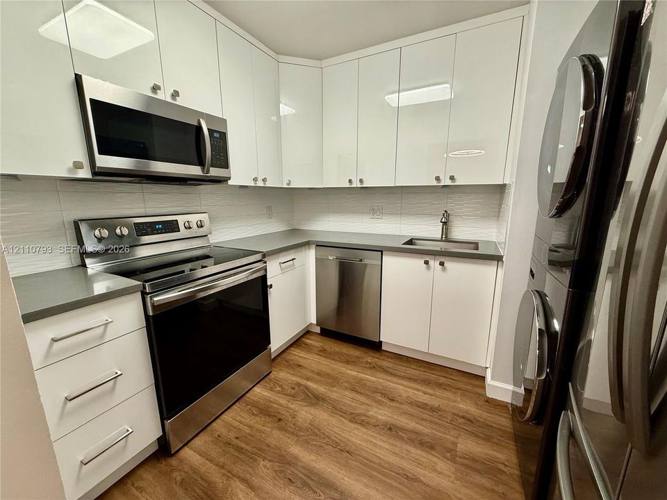 Kitchen featuring white high-gloss cabinetry, stainless steel appliances, solid-surface countertops, textured tile backsplash, and wood-finish flooring