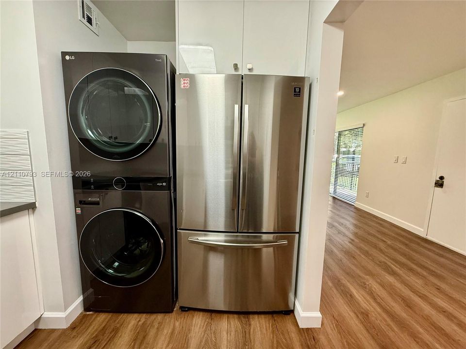 Stacked laundry unit, stainless steel refrigerator, white cabinetry, and wood-finish flooring