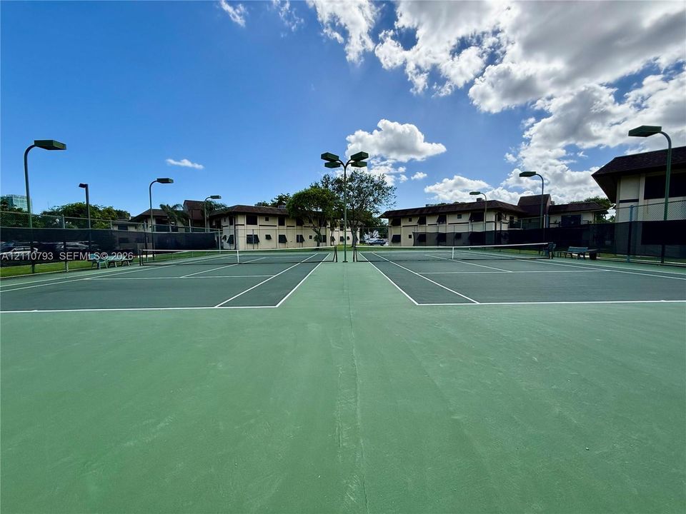 Dual hard-court tennis facility featuring perimeter fencing and overhead floodlighting
