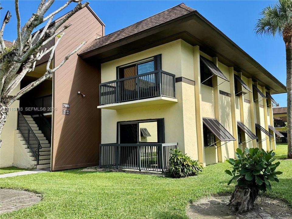 Two-story building exterior featuring a stucco façade, vertical wood-panel accents, metal window awnings, and private balconies with railings