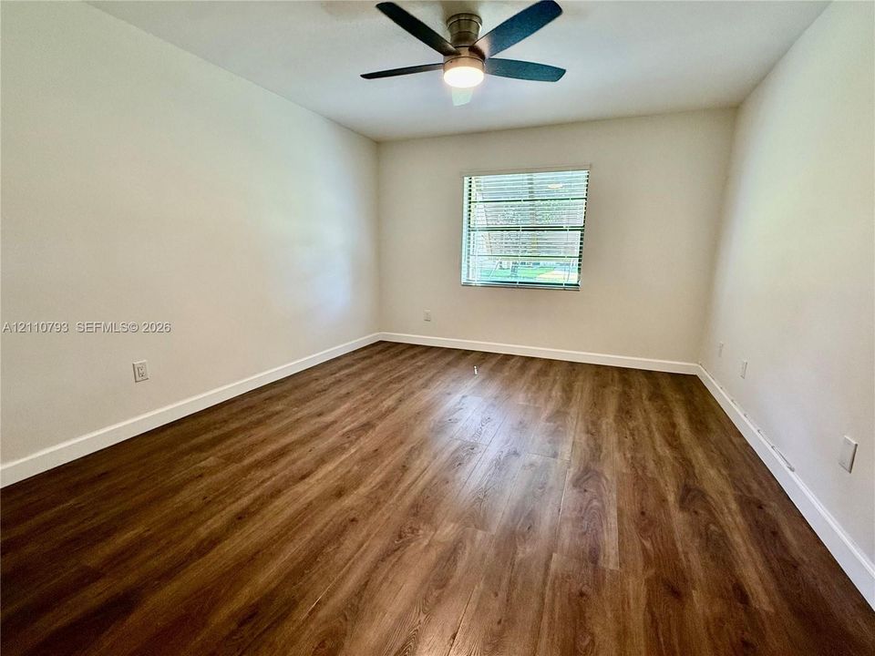 Neutral-toned walls paired with wood-finish flooring, featuring a central ceiling fan with integrated lighting and a window with horizontal blinds