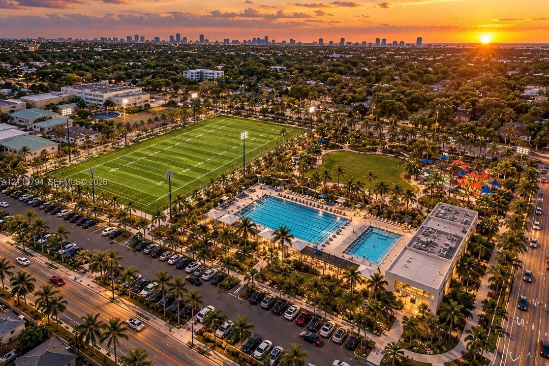 Aerial perspective of a multi-purpose recreational complex featuring a professional-grade athletic field, two swimming pools, structured parking, and extensive landscaping