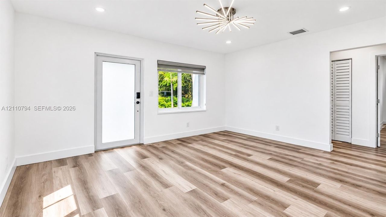 Wood-finish flooring, recessed lighting, modern sunburst chandelier, glass-paneled exterior door, and louvered closet door
