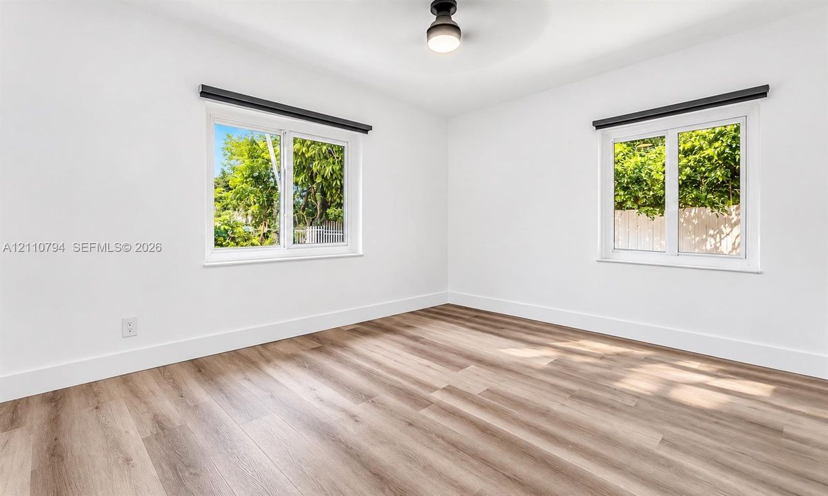 Room interior featuring light wood-finish flooring, dual windows with modern black hardware, and a contemporary flush-mount ceiling light fixture