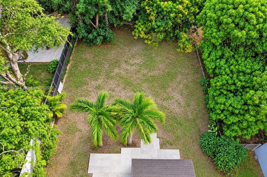 Expansive backyard featuring a stone-paver patio, mature landscaping, and palm trees enclosed by perimeter fencing