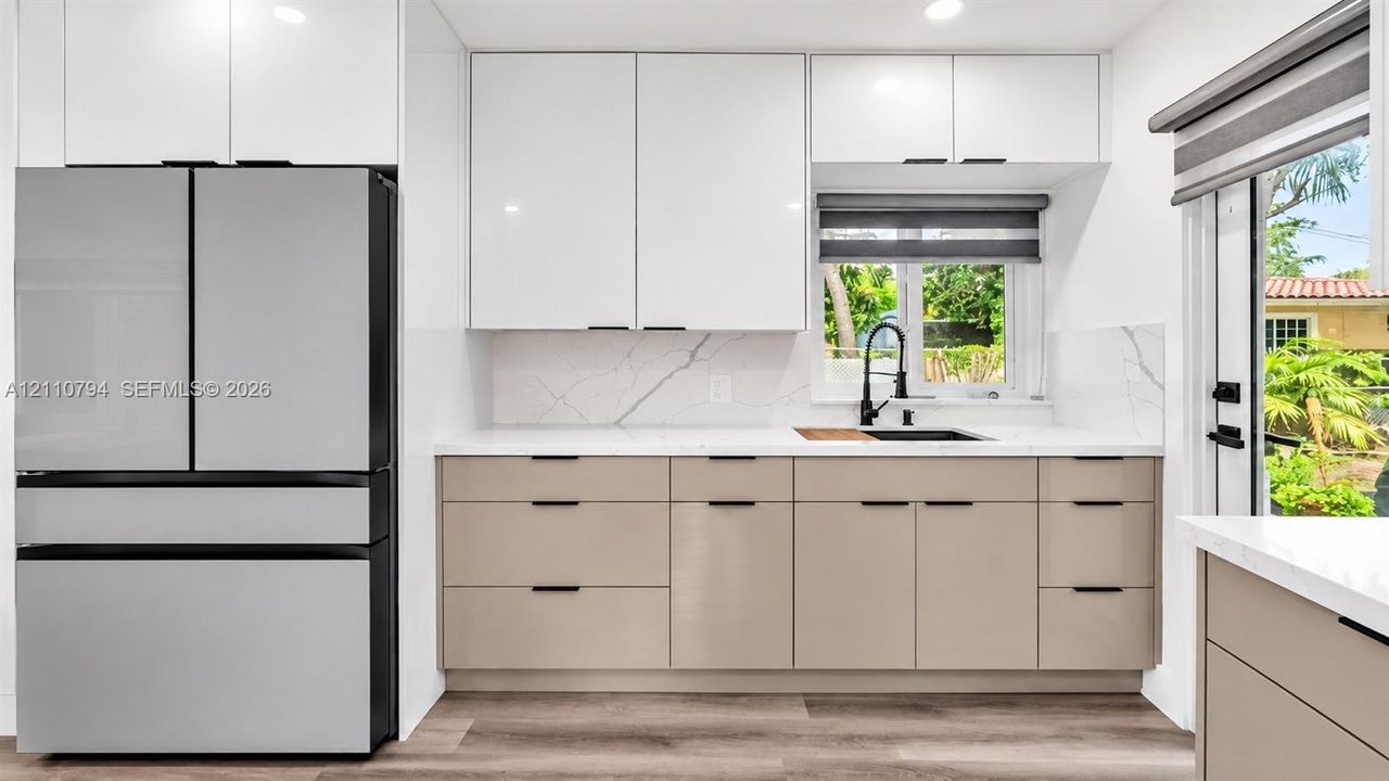 Kitchen featuring two-tone flat-panel cabinetry, white stone-patterned countertops, a matte black faucet with an integrated sink, and wood-finish flooring