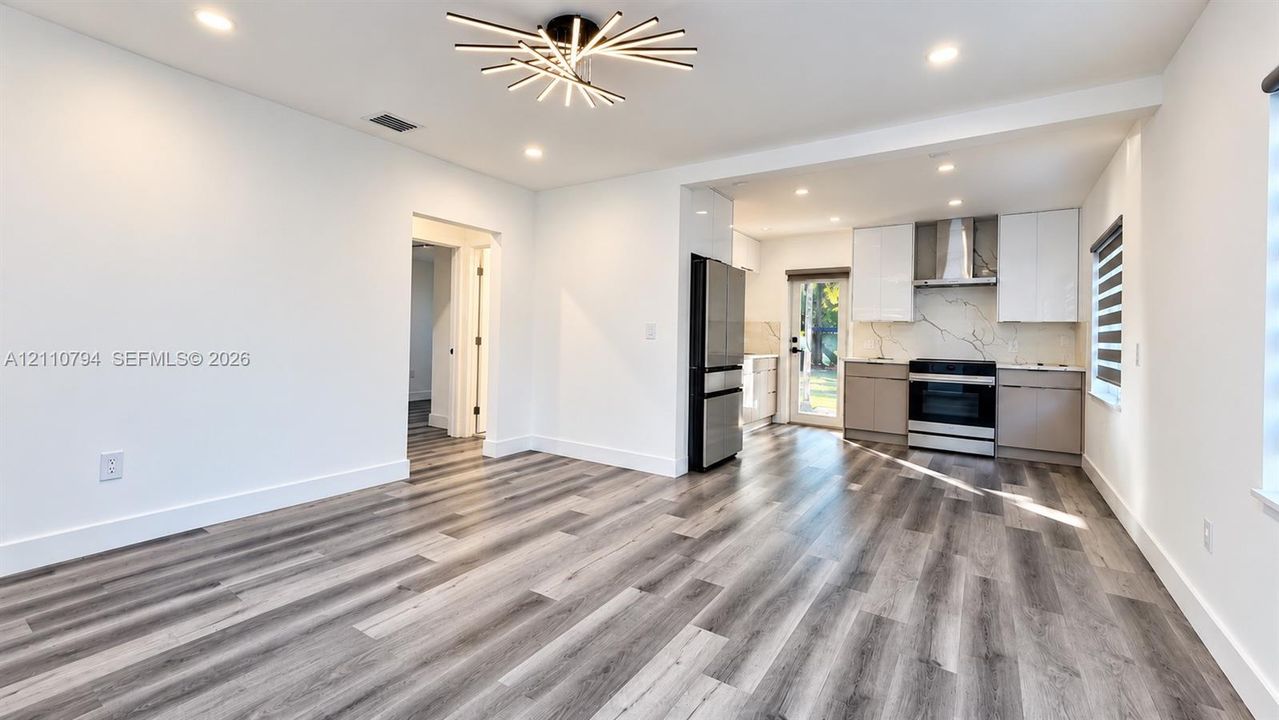 Modern kitchen featuring two-toned cabinetry, stainless steel appliances, stone-look backsplash, wood-finish flooring, and a contemporary multi-arm flush-mount light fixture