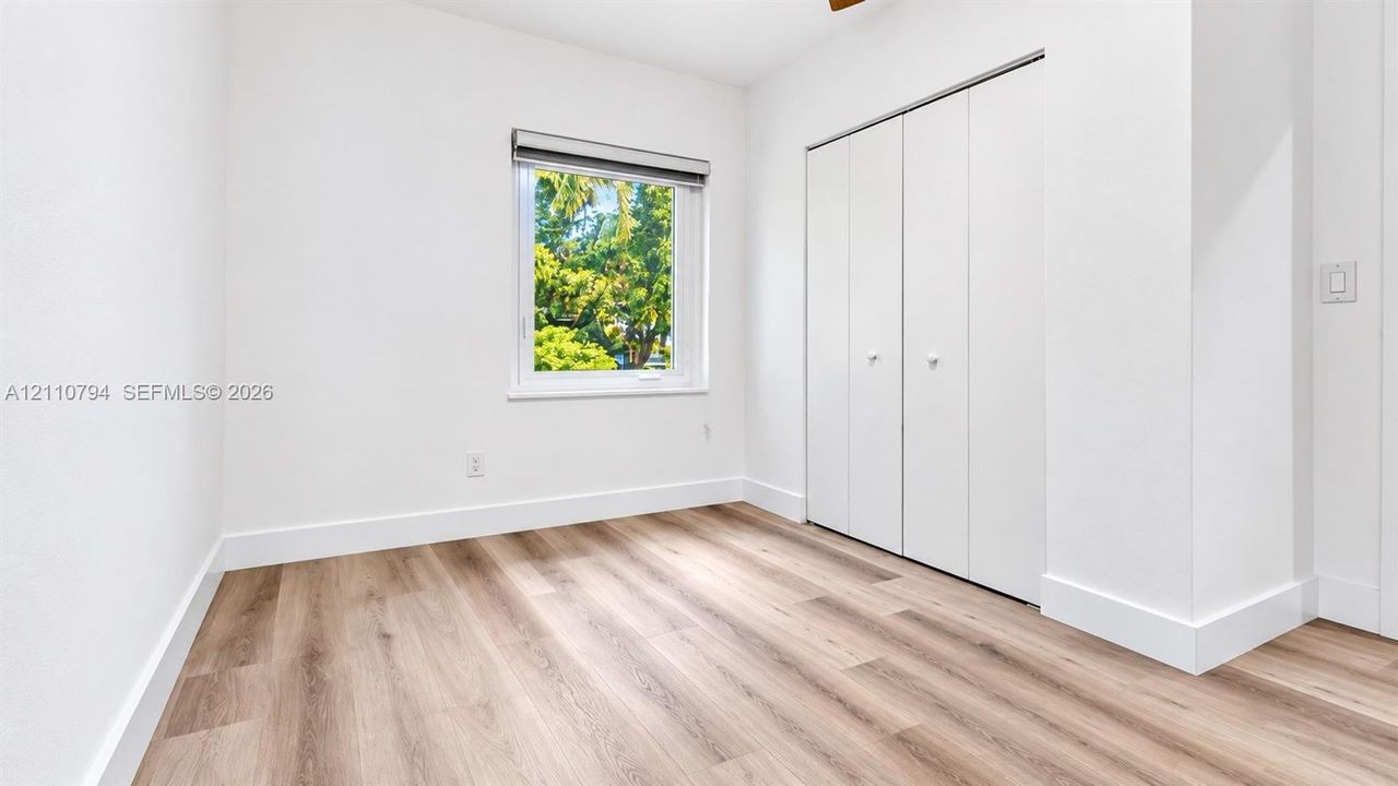 Bright interior space featuring wood-finish flooring, a single window, and a built-in closet with multi-panel folding doors
