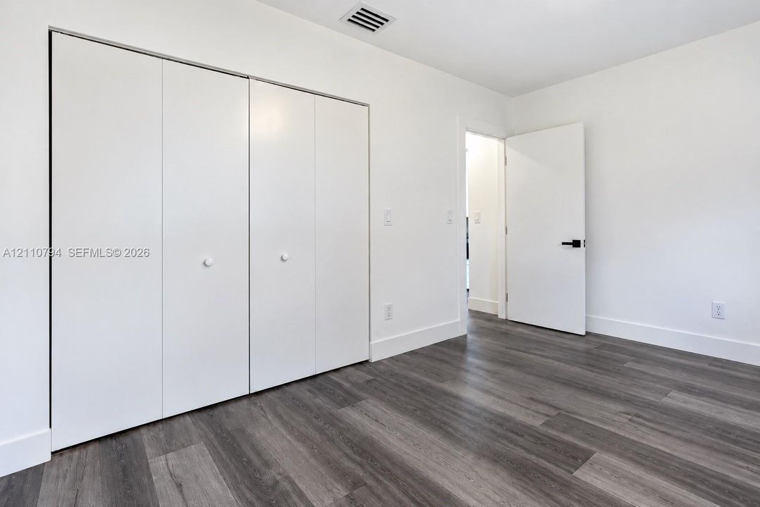 Wood-finish flooring, white walls, floor-to-ceiling bi-fold closet doors, and interior door with matte black hardware