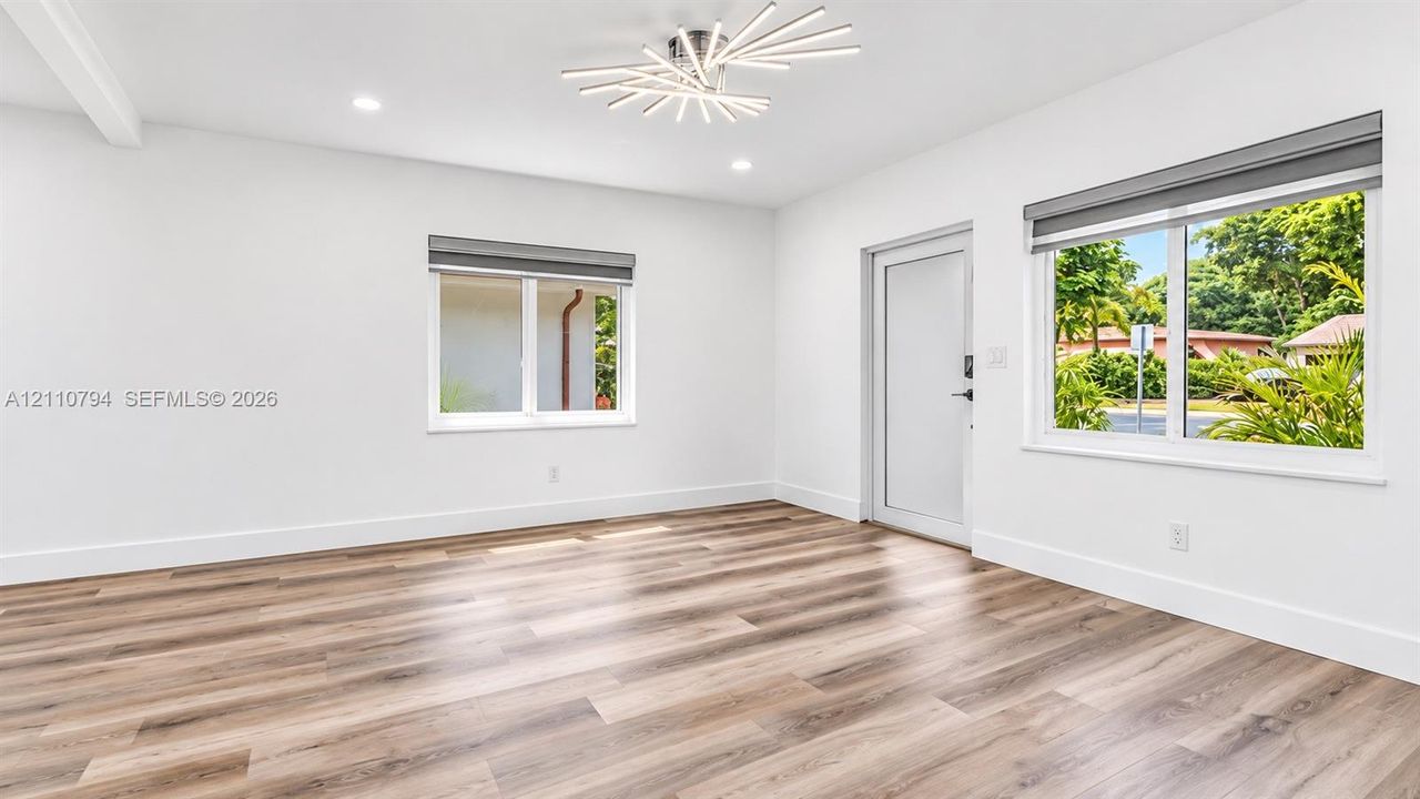 Interior featuring wood-finish flooring, recessed lighting, a modern starburst-style ceiling fixture, multi-pane windows with integrated blinds, and a glass-panel entry door