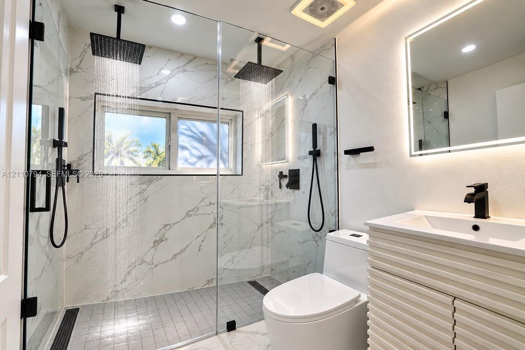 Walk-in shower with floor-to-ceiling stone-patterned tile, dual square rain-style shower heads, matte black plumbing fixtures, and textured-front vanity with integrated sink