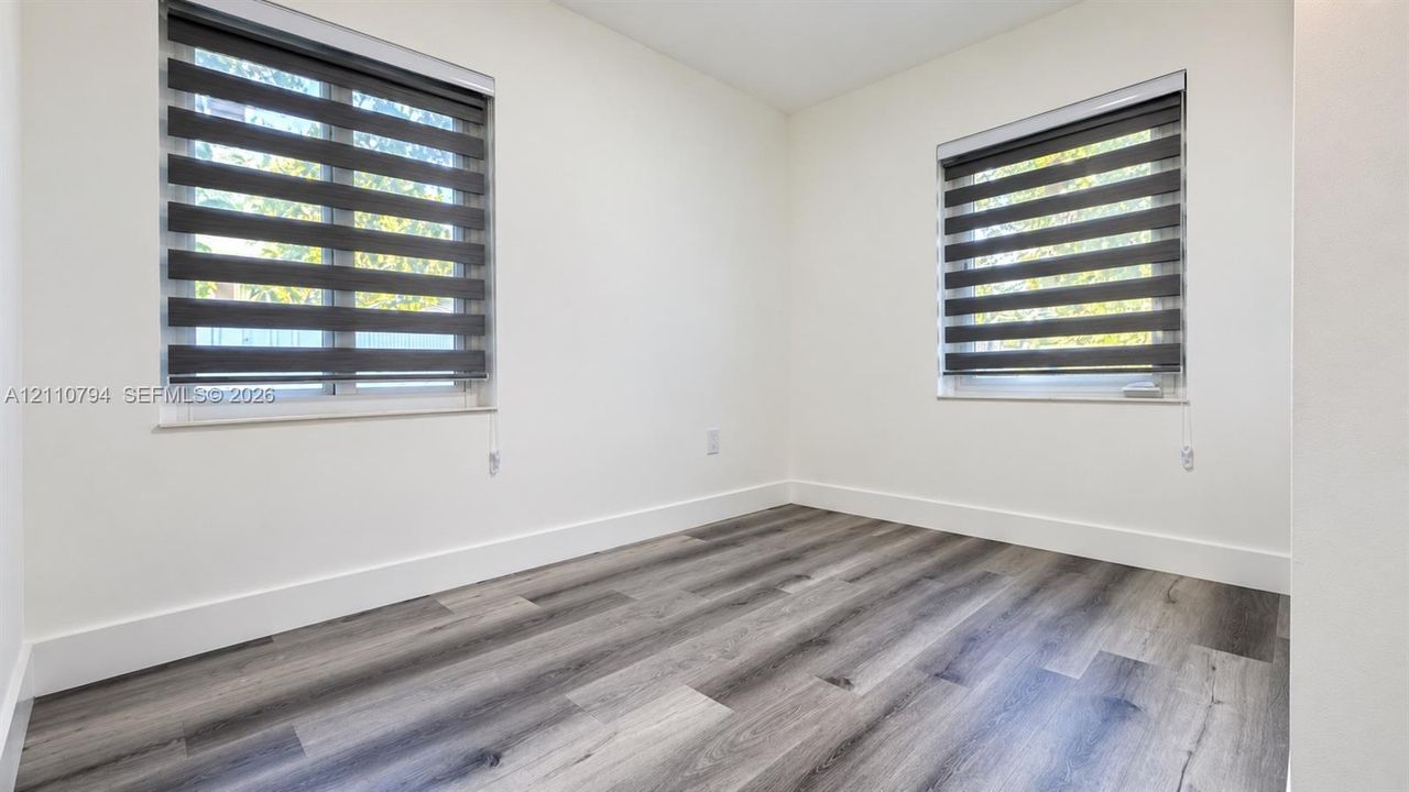 Neutral interior room featuring wood-finish flooring, two dual-pane windows, and adjustable dual-layer roller shades