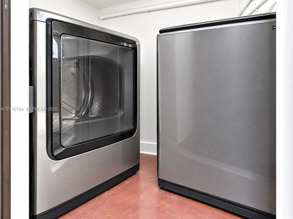 Laundry area featuring metallic-finish side-by-side appliances and neutral-toned flooring