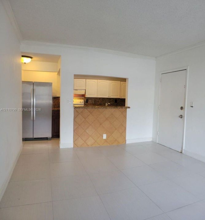 Kitchen featuring a pass-through opening, stone-finish countertops, tile-front breakfast bar, and stainless steel refrigerator, complemented by large-format floor tiling