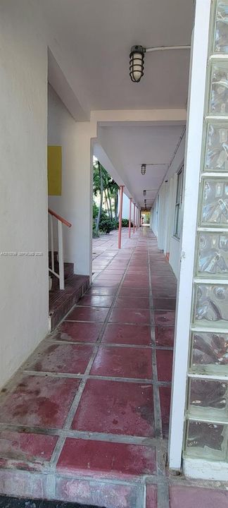Covered outdoor corridor featuring square tile flooring, vertical support pillars, glass block wall accents, and caged-style wall-mounted lighting