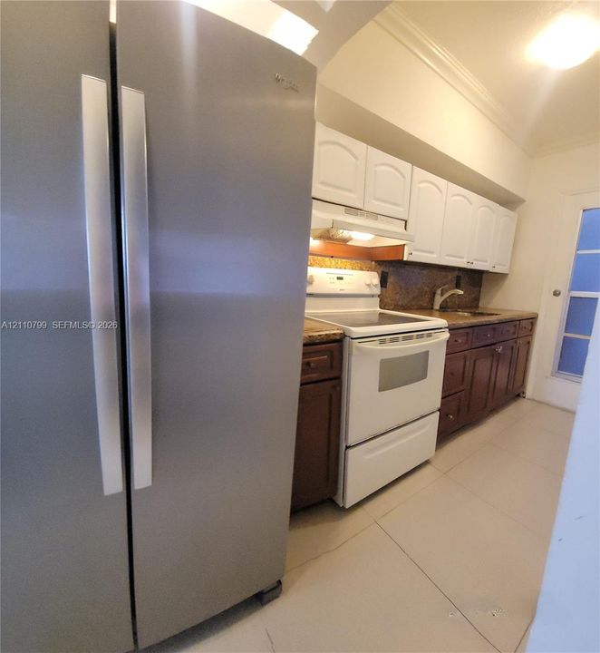 Kitchen featuring stainless steel side-by-side refrigerator, white appliance suite, dual-tone cabinetry, stone-finish countertops, and tile flooring