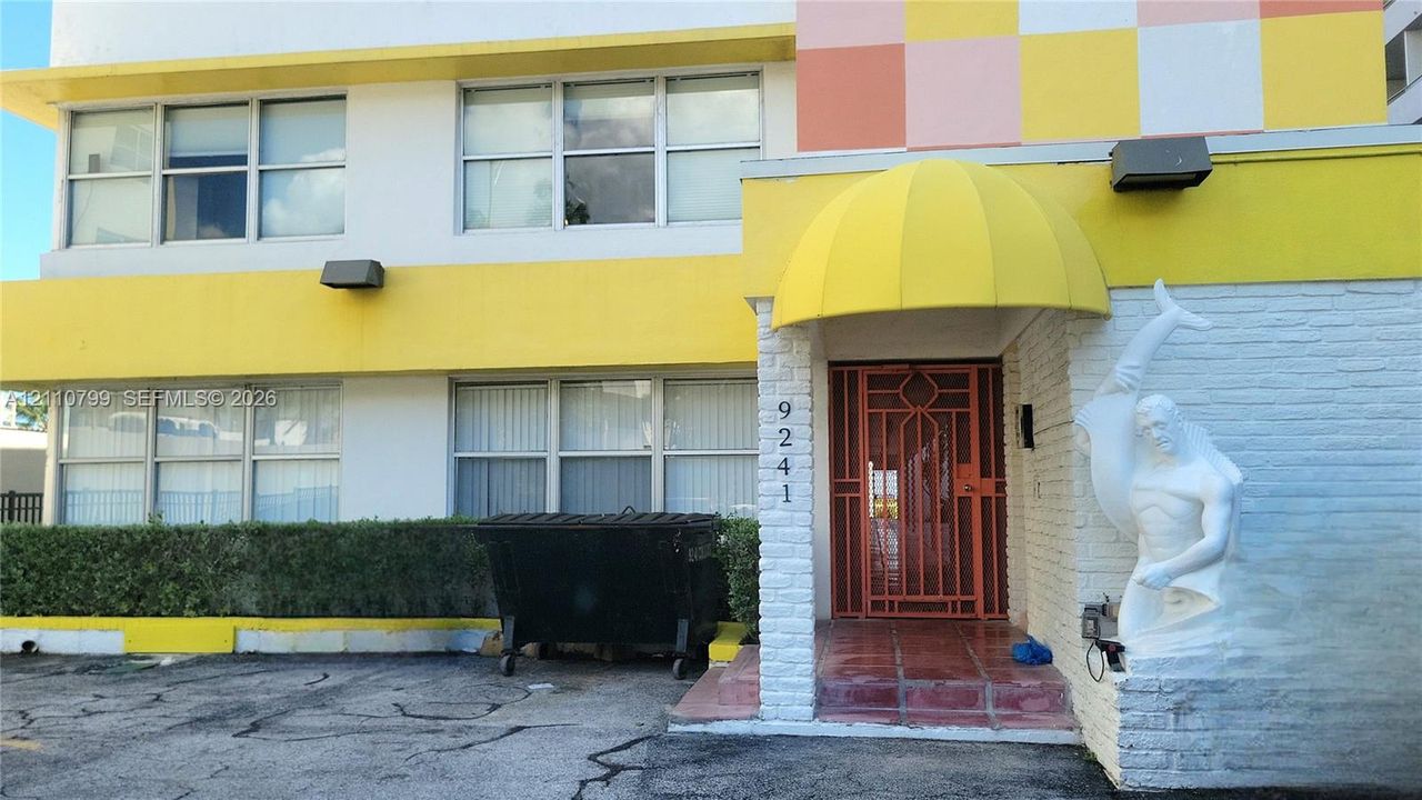 Exterior facade featuring a painted brick finish, multi-pane window configuration, arched entryway canopy, decorative sculptural masonry, and metal security gate