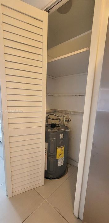 Utility closet featuring louvered bi-fold doors, tile flooring, and integrated white shelving