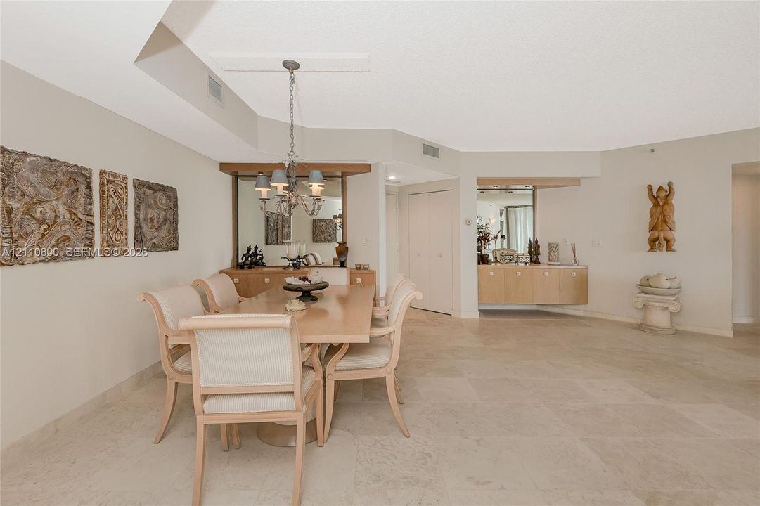 Open-concept dining area featuring large-format tile flooring, built-in cabinetry with mirror backing, a suspended multi-light chandelier, and additional integrated wall-mounted storage