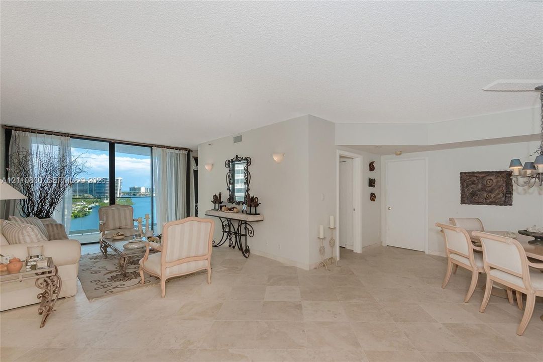 Open-concept living space featuring neutral stone-finish tile flooring, floor-to-ceiling glass sliding doors, and a multi-tiered crystal chandelier