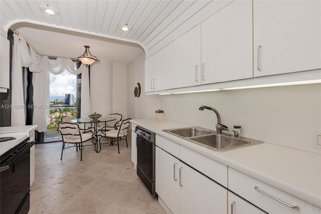 Kitchen featuring white cabinetry, solid-surface countertops, dual-basin stainless steel sink, under-cabinet lighting, and plank-style ceiling detail