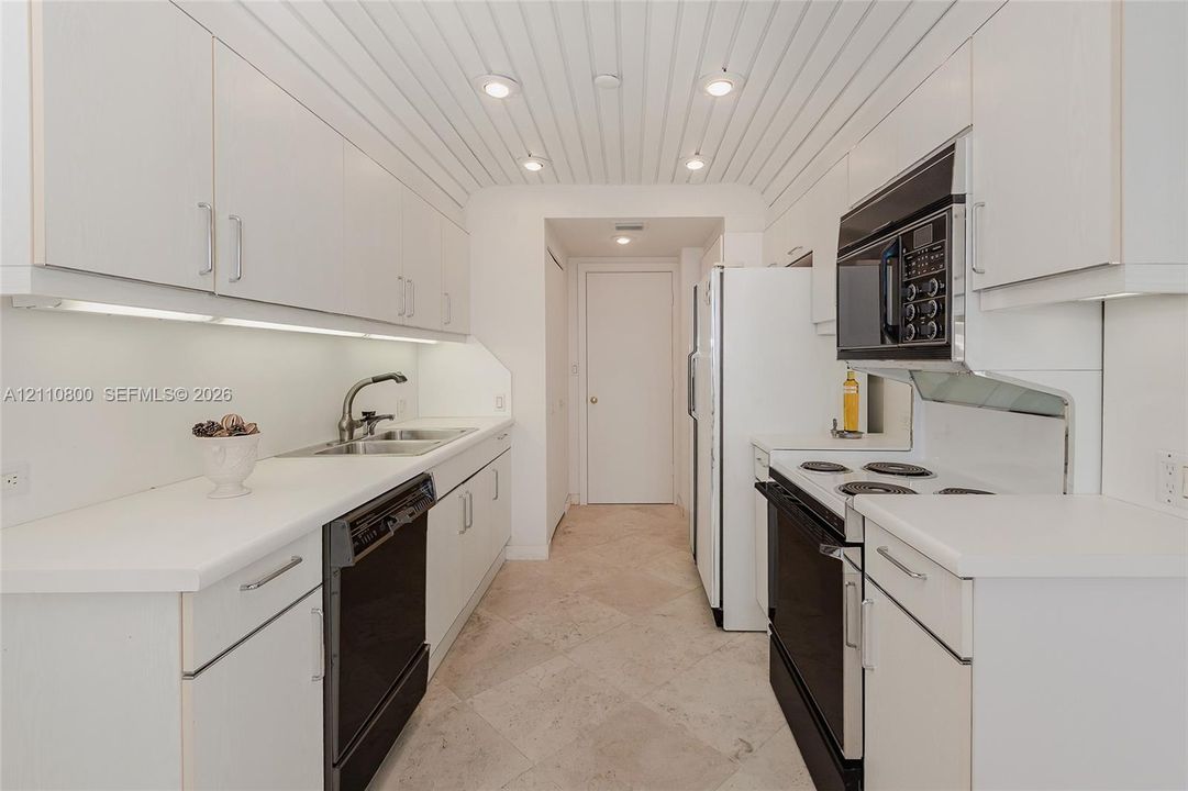 Galley kitchen featuring white cabinetry, under-cabinet lighting, a vertical-plank ceiling with recessed lighting, stone-tile flooring, and built-in appliances