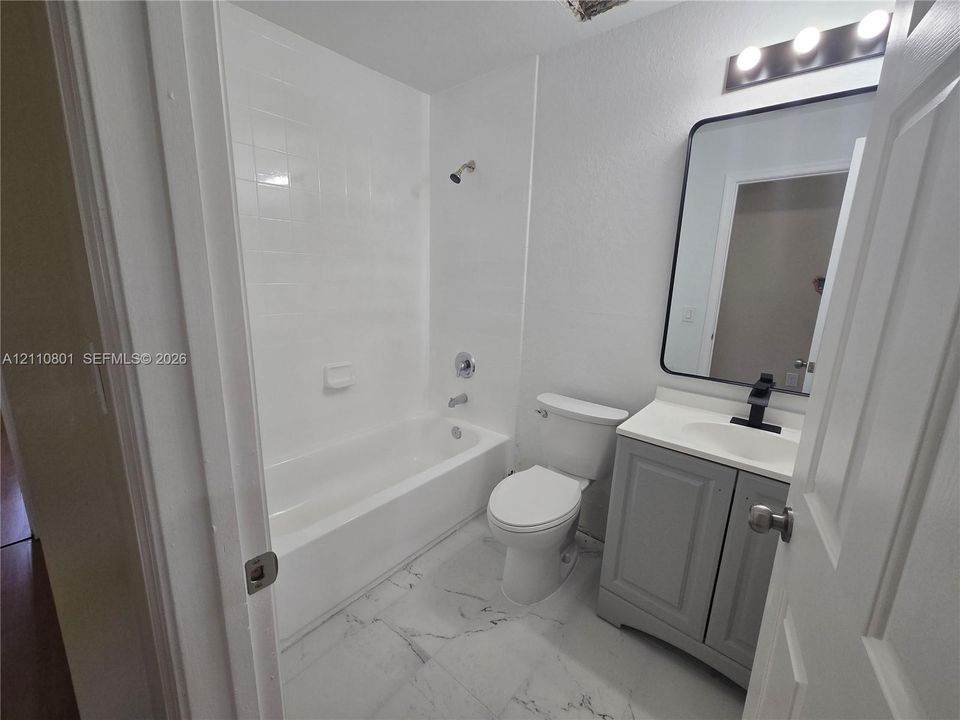 Bathroom featuring a vanity cabinet with white countertop, rectangular vessel sink, matte black hardware, arched wall mirror, and light-toned tile flooring