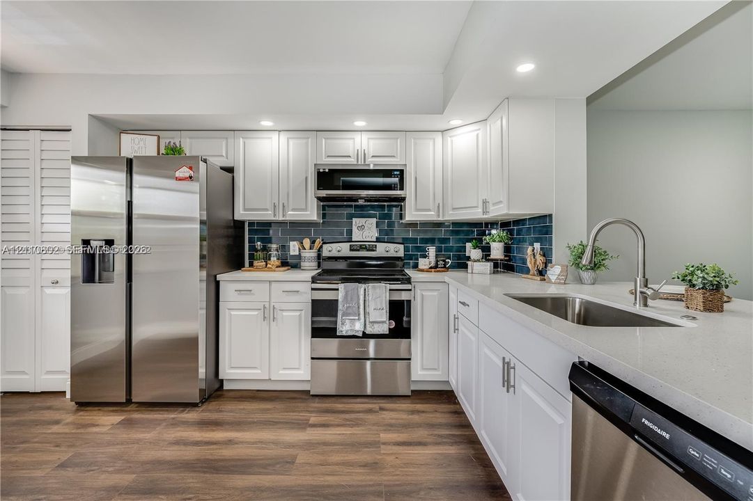 Kitchen featuring white shaker-style cabinetry, stainless steel appliances, dark subway-tile backsplash, stone-finish countertops, and wood-finish flooring