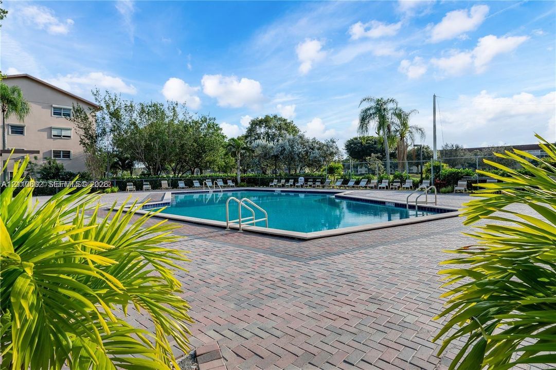 Outdoor swimming pool featuring a brick-paver deck, metal safety railings, and surrounding tropical landscaping