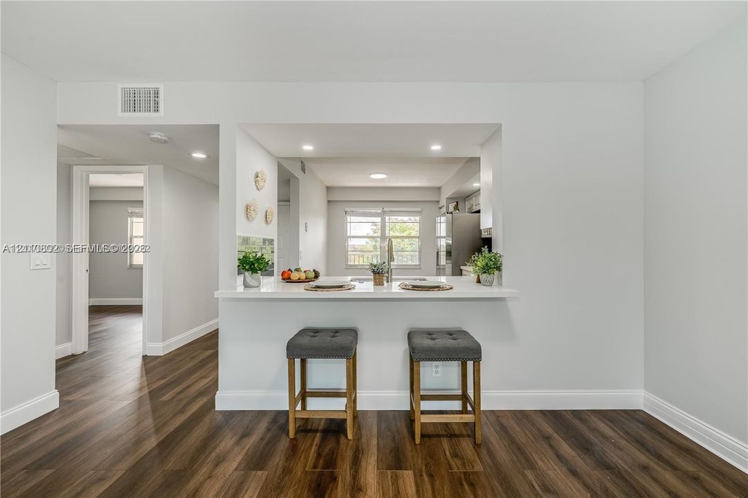 Kitchen featuring an open pass-through window with a quartz countertop breakfast bar, recessed lighting, and wood-finish flooring
