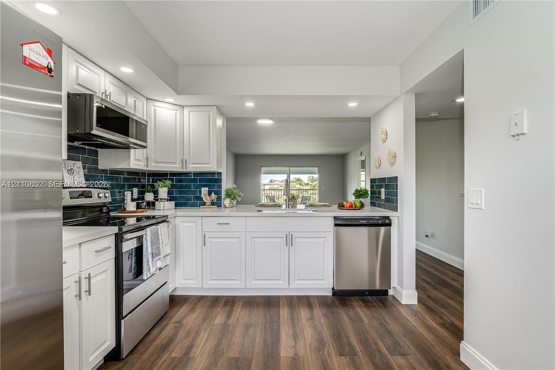 Kitchen featuring white shaker-style cabinetry, stainless steel appliances, dark subway tile backsplash, light-toned countertops, and wood-finish flooring