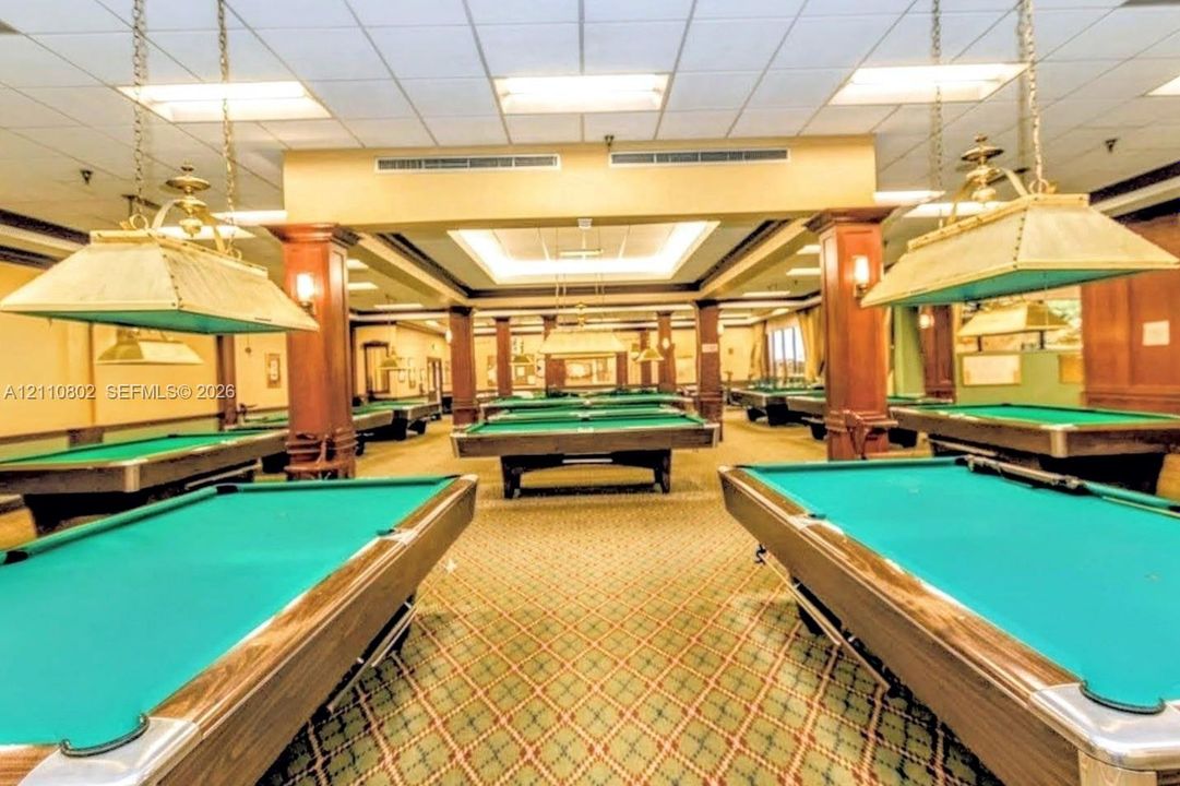 Spacious recreation room featuring recessed lighting, decorative wood columns, suspended task lighting, and a patterned carpeted floor