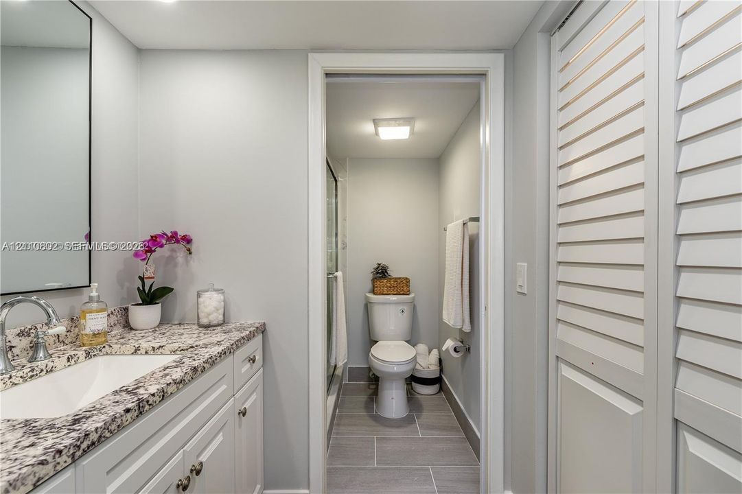 Vanity featuring a stone-look countertop, integrated sink with chrome faucet, framed mirror, and louvered closet doors
