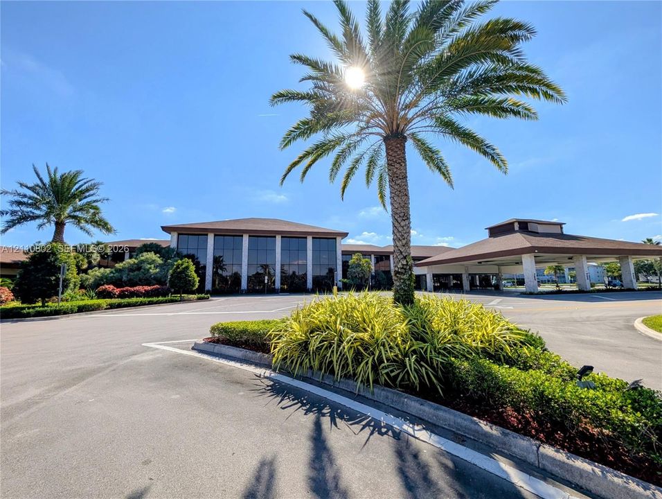 Commercial property exterior featuring a multi-story glass-paneled facade, extended porte-cochère, paved asphalt surface, and landscaped grounds with mature palm trees