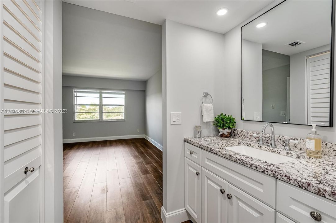 Vanity featuring white shaker-style cabinetry, stone-finish countertop with an integrated rectangular basin, and a framed mirror