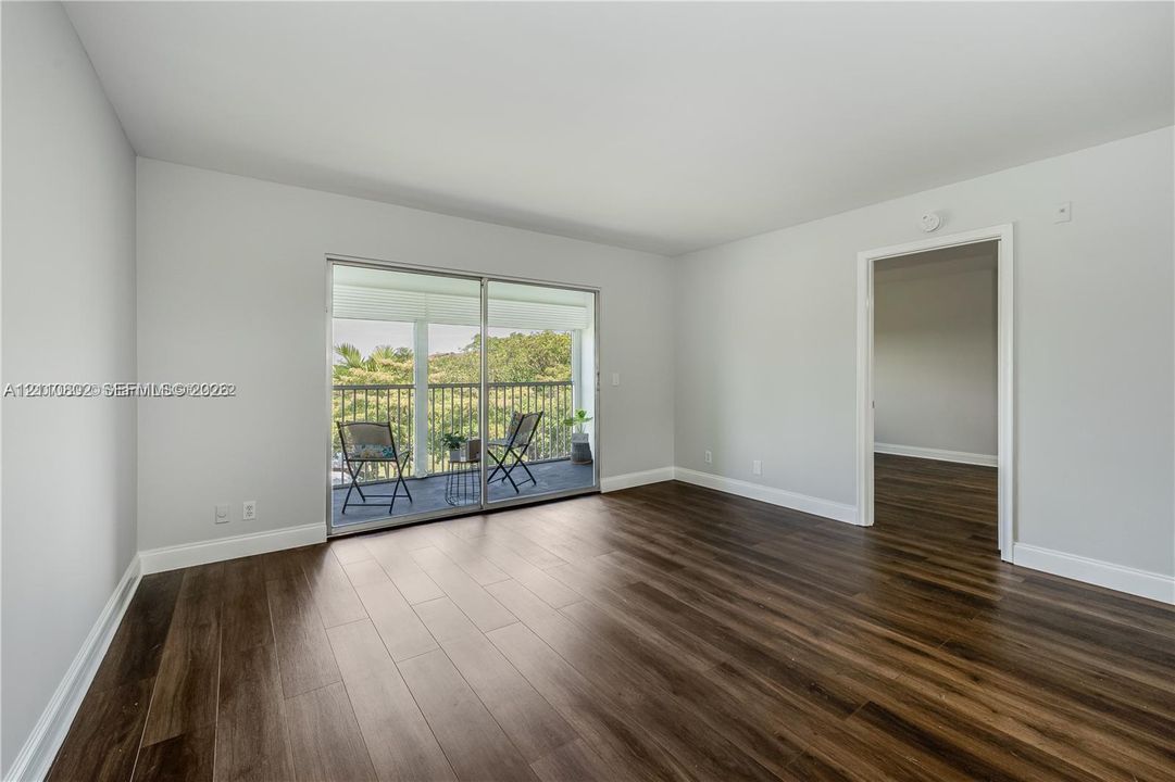 Interior room featuring wood-finish flooring, neutral wall tones, and sliding glass doors opening to an exterior balcony