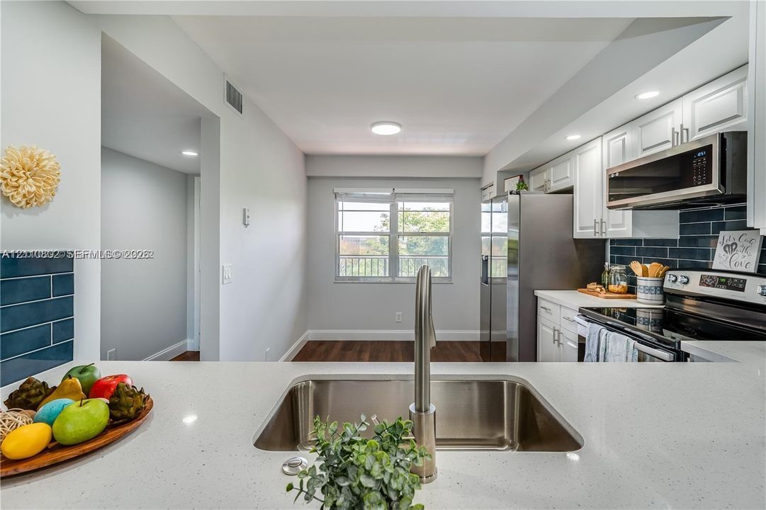 Kitchen featuring a quartz countertop, stainless steel under-mount sink, white shaker-style cabinetry, dark tiled backsplash, and wood-finish flooring