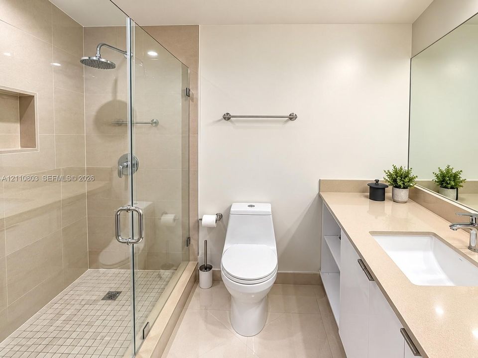 Bathroom featuring a walk-in shower with a glass enclosure, rainfall showerhead, and integrated wall niche, complemented by a vanity with a solid-surface countertop and a large wall-mounted mirror