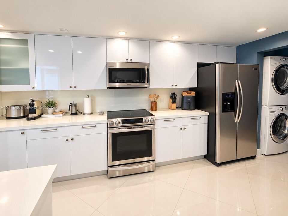 Contemporary kitchen featuring high-gloss white cabinetry, solid-surface countertops, stainless steel appliances, and large-format tile flooring, complete with a built-in laundry station