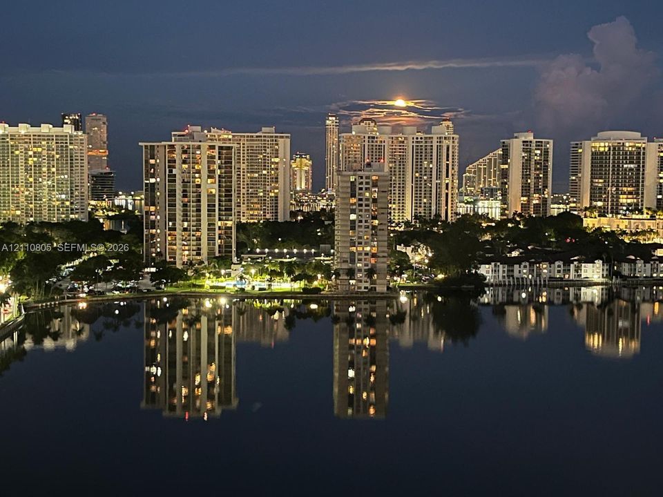 Panoramic cityscape featuring high-rise architecture, expansive water frontage, and reflections across the water surface