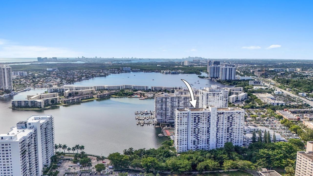 Aerial perspective of high-rise building situated on a peninsula, featuring immediate water frontage, deep-water marina, and tropical landscaping