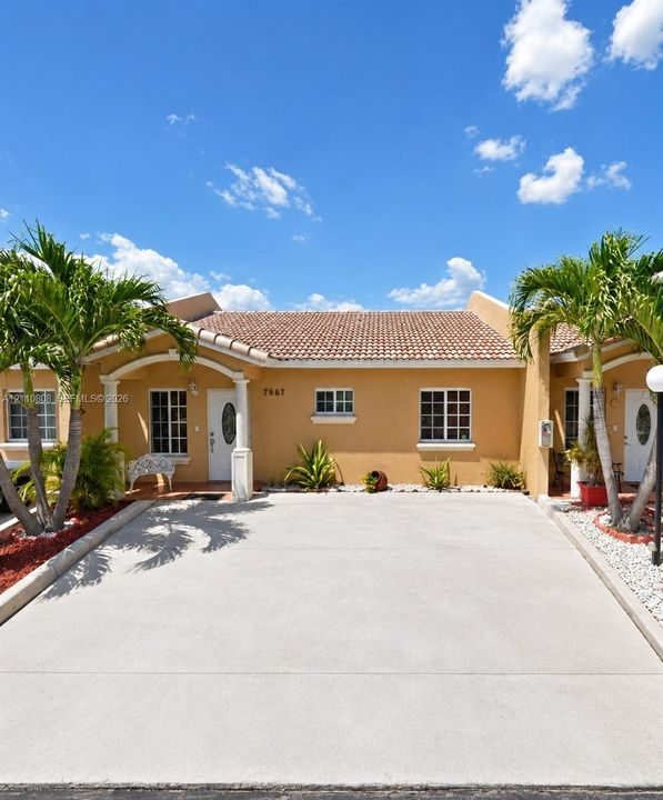 Stucco exterior featuring a clay tile roof, arched entryway with decorative columns, and a concrete driveway