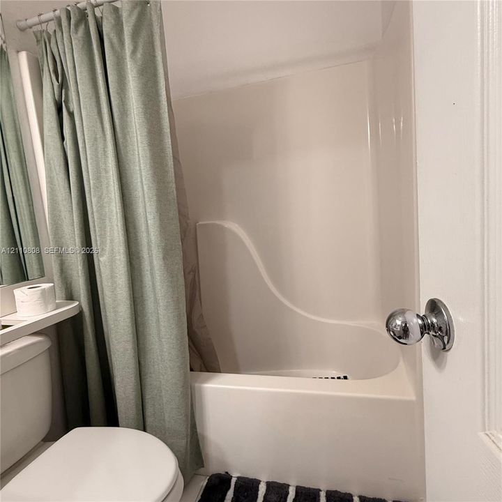 Integrated white acrylic tub and wall surround featuring a chrome-finish door knob