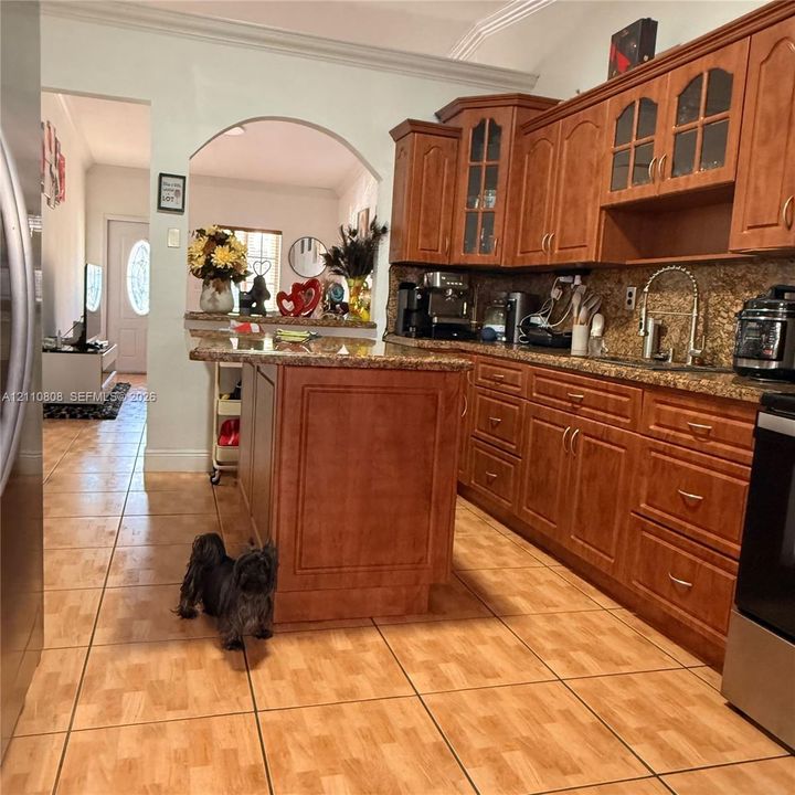 Kitchen featuring stained wood cabinetry, stone countertops, central island, tiled flooring, and arched entryway