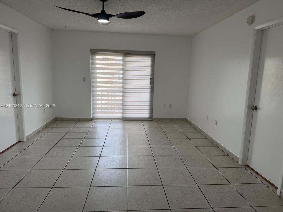 Interior room featuring tile flooring, a modern three-blade ceiling fan, and sliding glass doors with adjustable roller shades
